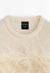 Pull en maille crème avec garniture en plumes duveteuses sur la poitrine, doté d'un col rond et d'une étiquette noire Massimo Dutti Studio à l'intérieur du col.