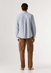 Camicia a maniche lunghe a righe di colore azzurro chiaro con colletto bottonato, abbinata a pantaloni cargo marroni con tasche laterali e design a gamba affusolata.