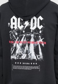 Čierna mikina s kapucňou s bielym logom AC/DC, grafikou koncertnej scény, červeným textom "ROCK OR BUST WORLD TOUR" a časovým rozmedzím 2015-2016.
