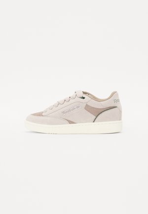 Sneaker beige pallido in suede, dotate di collare imbottito, lacci rotondi, un'accensione verde sul lato e suola in gomma testurizzata.
