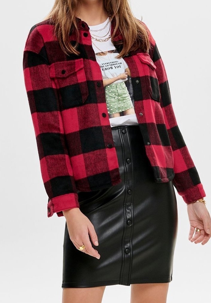 Chemise en flanelle à carreaux rouge et noir avec deux poches frontales, associée à une jupe crayon en similicuir noir avec des détails de boutons.