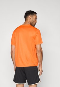 Camiseta deportiva de manga corta en naranja brillante, confeccionada con un tejido que absorbe la humedad y tiene una textura suave, con un diseño clásico de cuello redondo.
