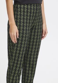 Pantalons à motifs noir et vert avec un design en damier, présentant un tissu texturé et une coupe slim au niveau des jambes.