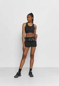Top corto atlético negro y pantalones cortos, con una tela suave y un diseño ajustado. Incluye una bolsa de cintura negra con detalles reflectantes.