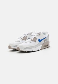 Nike tenisice s bijelim i svijetlosivim dizajnom, s plavim swooshom, teksturiranim gornjim dijelom i podebljanim đonom s vidljivom zračnom jedinicom.