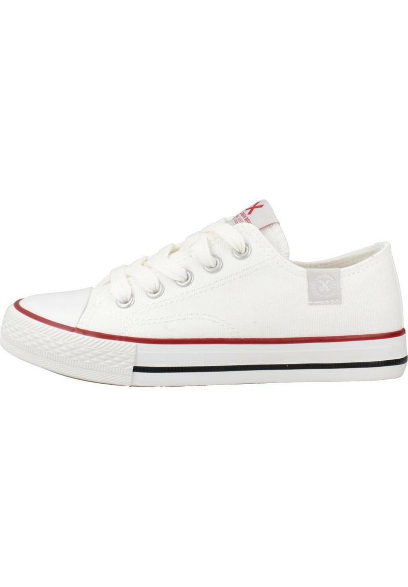 Sneakers bianchi in canvas con punta in gomma, accenti rossi sulla suola, lacci piatti e un'etichetta con logo sul lato. Design classico a basso profilo.
