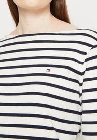 Randig långärmad tröja med marinblå och vita horisontella ränder, vid halsringning och en liten logga på bröstet. Mjuk bomullstyg.