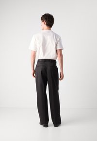 Schwarze Hose mit geradem Schnitt, glattem Stoff und zwei Gesäßtaschen. Getragen mit einem schlichten weißen kurzärmeligen Hemd. Einfaches Design.