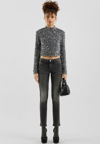 Srebrny krótki top z cekinami i długimi rękawami, w połączeniu z dopasowanymi czarnymi jeansami. Czarna torebka, buty na platformie z błyszczącym detalem.