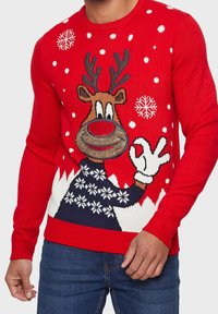 Pull en tricot rouge avec un motif de renne, des antlers, un grand nez et des accents de flocons de neige. Comprend un col et des poignets côtelés.
