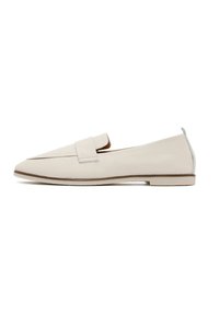 Mocassin beige en cuir à enfiler avec une semelle plate et un détail de bride cousue sur le dessus, présenté de profil sur un fond blanc.