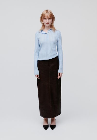 Jasnoniebieska, prążkowana, długorękawowa koszula polo połączona z ciemnobrązową, skórzaną spódnicą maxi. Modelka nosi czarne szpilki w szpic. Proste tło.