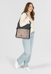 Handtasche aus dunkelblauem Textilmaterial mit einem hellbeigen Einsatz, der ein bedrucktes Design aufweist. Inklusive verstellbarer Träger und goldenen Akzenten.