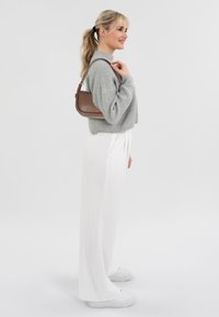 Maglione grigio a maglia, pantaloni bianchi a gamba larga e sneakers bianche. Borsa a tracolla marrone con forma curvata. Texture liscia e design minimalista.