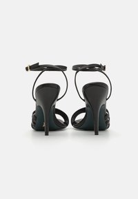 Schwarze High-Heel-Sandalen mit schmalen Knöchelriemen, offener Zehenpartie und Kreuzdetails über dem Spann. Glatte Lederoberfläche.