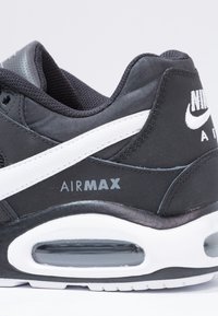 Zwarte sneaker met een gevoerde grijze kraag, witte swoosh-accent, zichtbare luchtkussens en "AIR MAX" branding in het grijs op de zijkant.