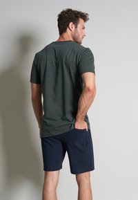 Tricou scurt cu mânecă, de culoare verde închis, cu decolteu ribat, asortat cu pantaloni scurți de culoare bleumarin, cu un buzunar lateral, ambele dintr-un material moale.