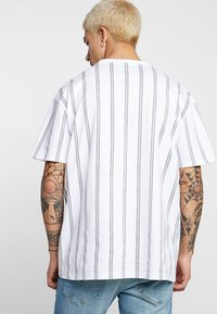White t-shirt with vertical black stripes, short sleeves, and a crew neckline. Features a relaxed fit and smooth cotton texture.