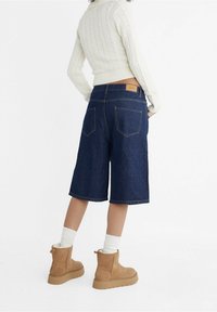 Dark denim culotte shorts with a mid-rise waist, back pockets, and a leather patch. Paired with a knitted cream sweater and tan ankle boots.