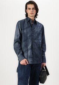 Camicia a motivi navy con colletto botton-down, tessuto testurizzato, caratterizzata da design astratti, abbinata a pantaloni coordinati e una borsa nera.