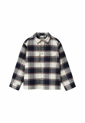 Camisa de manga larga con botones, patrón de cuadros en negro, blanco y gris, y dos bolsillos frontales en el pecho con botones.