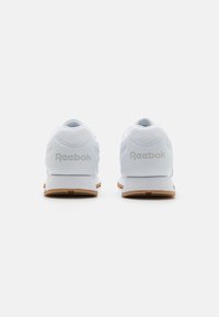 Biele tenisky Reebok s textúrovaným sieťovým zvrškom, hladkou gumovou podrážkou a gumovým vonkajším podošvou. Obsahuje mäkký golier okolo päty a logo na zadnej strane.