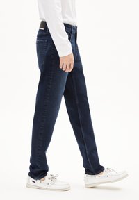 Donkerblauwe rechte spijkerbroek met een gladde textuur, vijf-pocket ontwerp en een tailleband met een subtiele merklogo. Gemaakt in combinatie met witte schoenen.