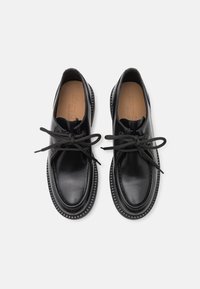 Une paire de chaussures de ville en cuir noir à lacets, avec des orteils arrondis et des semelles intérieures marron sur un fond blanc.