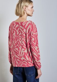 Losse trui in roze en beige met dierenprint, lange mouwen en zachte textuur. Gestyled met donkerblauwe jeans.