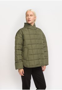 Oliven grøn pufferjakke med høj krave, quiltet design, lange ærmer og sidelommer. Blødt stof med en glat tekstur.