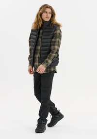 Schwarze Puffer-Weste, grün karierte Hemdbluse, schwarze Cargo-Hosen und schwarze Sneakers. Glatter Stoff, gesteppter Entwurf und funktionale Taschen.