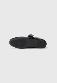Sapato de couro preto com uma forma ligeiramente curva, apresentando uma sola de borracha texturizada e uma correia ajustável para um ajuste seguro.