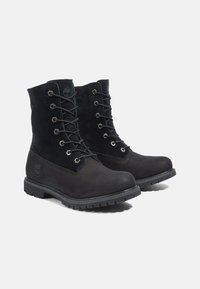 Botas de tobillo de cuero negro y ante con seis ojales de metal, diseño de cordones, cuello acolchado y suela de goma texturizada.