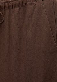 Gros plan sur un tissu marron montrant une taille élastique et une ouverture de poche sur un pantalon ou un short décontracté.