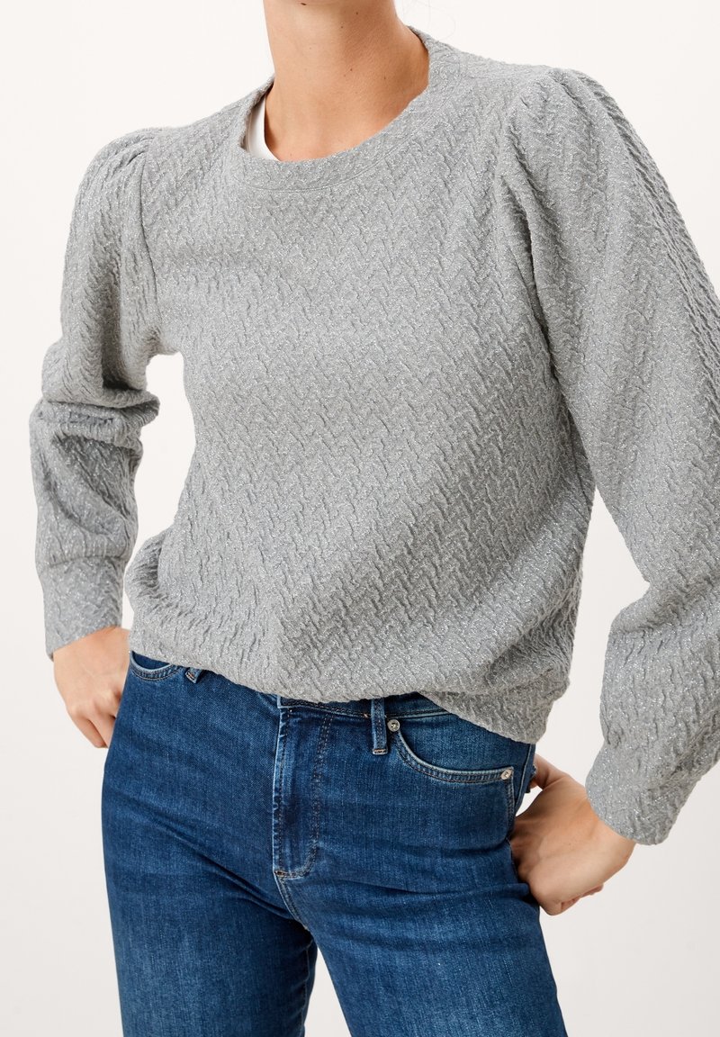 Grau strukturierter Pullover mit Fischgrätenmuster, Puffärmeln und Rundhalsausschnitt, kombiniert mit dunkelblauen Jeans.