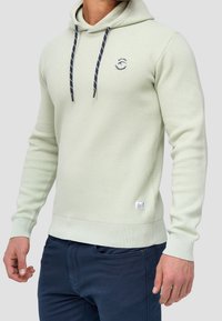 Sudadera verde claro con tejido texturizado, cierre de cordón con acentos en azul marino y un pequeño logo en el lado izquierdo del pecho.