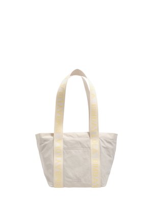 Beige tote bag with two wide cream handles featuring yellow "BIMBA Y LOLA" text, front pocket, and a smooth fabric texture.