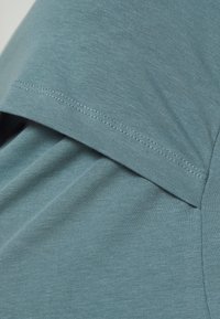 Krátký rukáv košile z měkké, texturované látky. Světle tyrkysová barva s žebrovaným vzorem a viditelným švem kolem límce a okrajů rukávů.