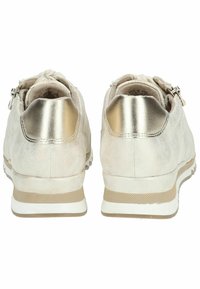 Beżowe buty sportowe z metalicznymi złotymi akcentami, gładką teksturą zamszu, niskoprofilowym designem i białymi gumowymi podeszwami z teksturowanym bieżnikiem.