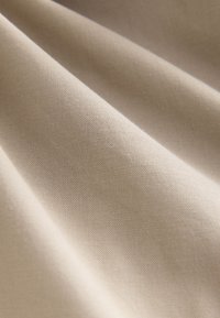 Glatter beiger Stoff mit feiner gewebter Textur und weichen Falten, die sanfte Schatten erzeugen.