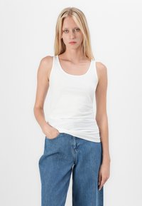 Witte katoenen tanktop met een ronde hals, gecombineerd met lichtblauwe denim jeans. De top heeft een strak ontwerp en een gladde textuur.