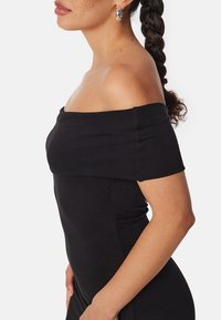 Robe noire décolletée, à la coupe près du corps, avec une texture lisse et des manches courtes. Remarquable par son style simple et classique.
