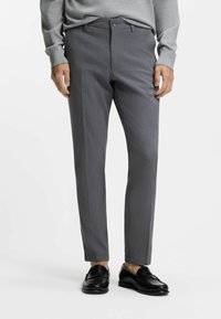 Gray tailored pants with a subtle texture, flat front, and side pockets, paired with black loafers, worn with a gray sweater.
