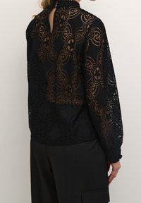 Schwarze Spitzenbluse mit floralen Mustern, langen Ärmeln, hohem Kragen und einem Schlüsselspalten-Design hinten. Die Textur ist durchsichtig mit detaillierten Verzierungen.