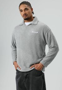 Grijze fleece trui met een kraag, voorzien van een zachte textuur en een wit geborduurd logo op de borst. Lange mouwen en een casual pasvorm.