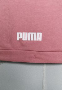 Gros plan d'une personne portant un sweat-shirt rose Puma et des leggings gris clair, affichant le logo Puma sur le sweat-shirt.