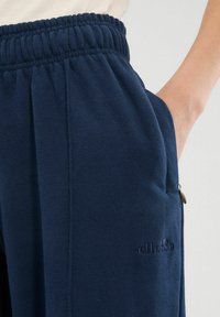 Donkerblauwe joggers van zachte stof, met een elastische tailleband, zijzakken en een klein geborduurd logo op de dij.