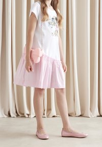 Biała koszulka z kwiatową grafiką, połączona z warstwową różową spódnicą z tiulu. Różowa torebka w kształcie kokardy oraz dopasowane różowe baletki.