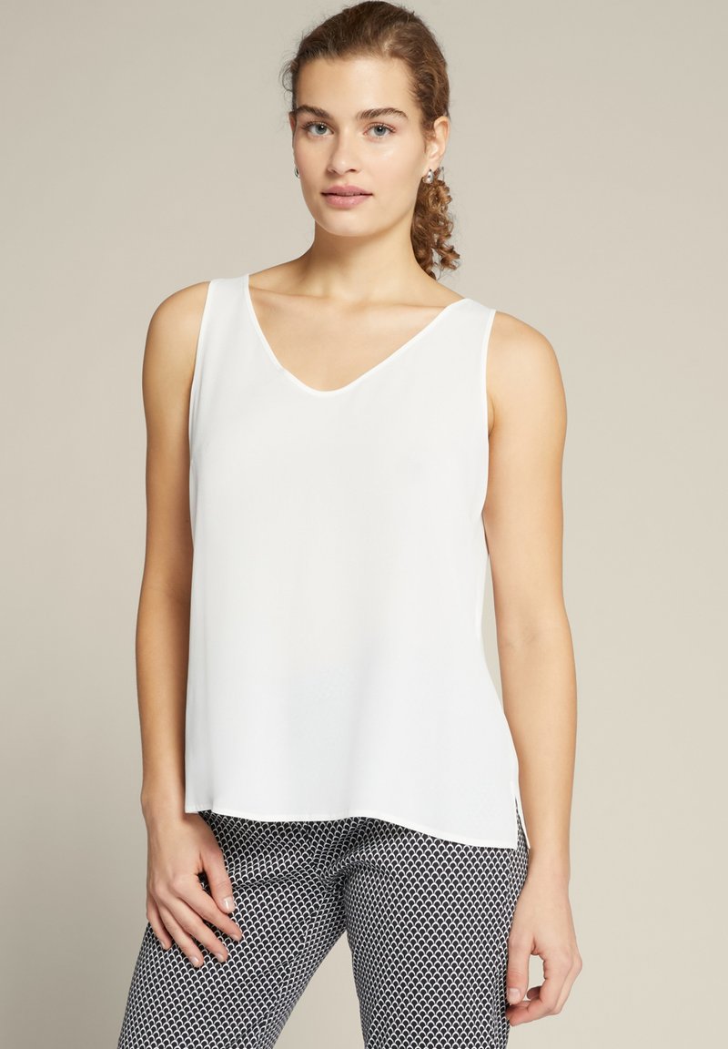 Witte mouwloze top met een V-hals, gladde stof, rechte snit en zijsplitten, gecombineerd met zwart-witte gestreepte broek.