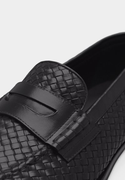 Mocassin en cuir noir avec une texture tissée et une bande en cuir lisse sur le devant, doté de coutures détaillées et d'un bout arrondi.